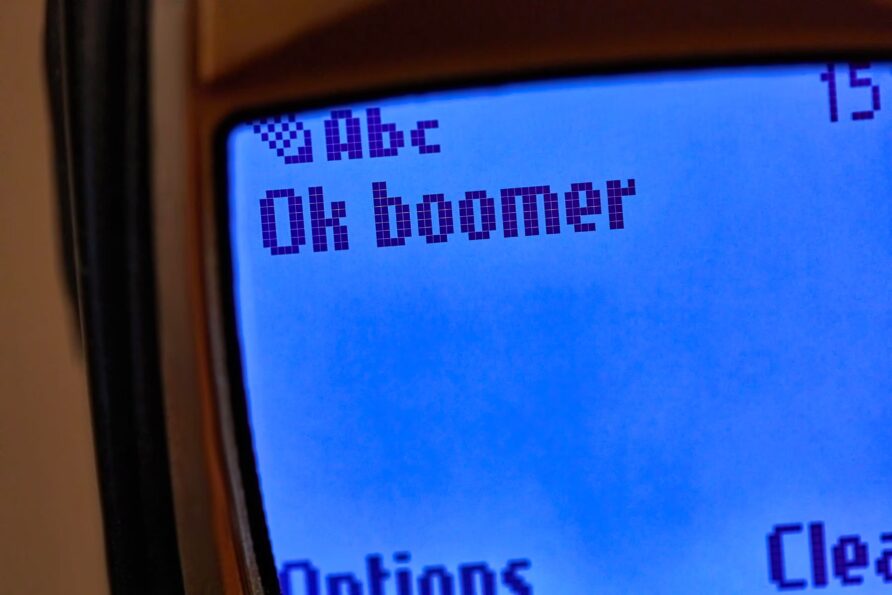 Schermo di un vecchio cellulare mostra il testo « Ok boomer » in pixel grandi.