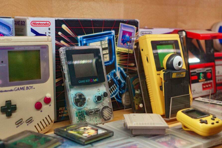 Diversi vecchi Game Boy, cartucce di giochi e una Game Boy Camera esposti su un tavolo.