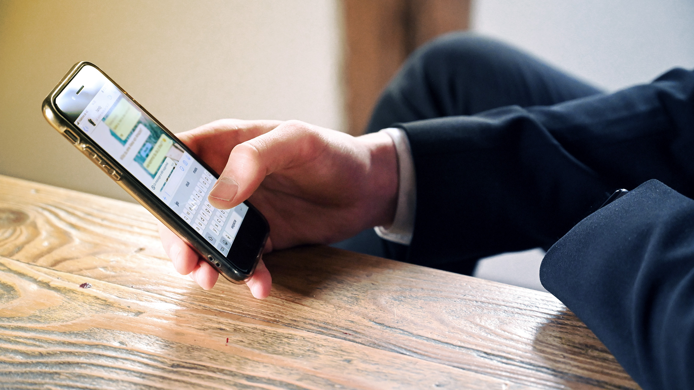Une main tient un smartphone sur un fond vert clair avec le logo WhatsApp.