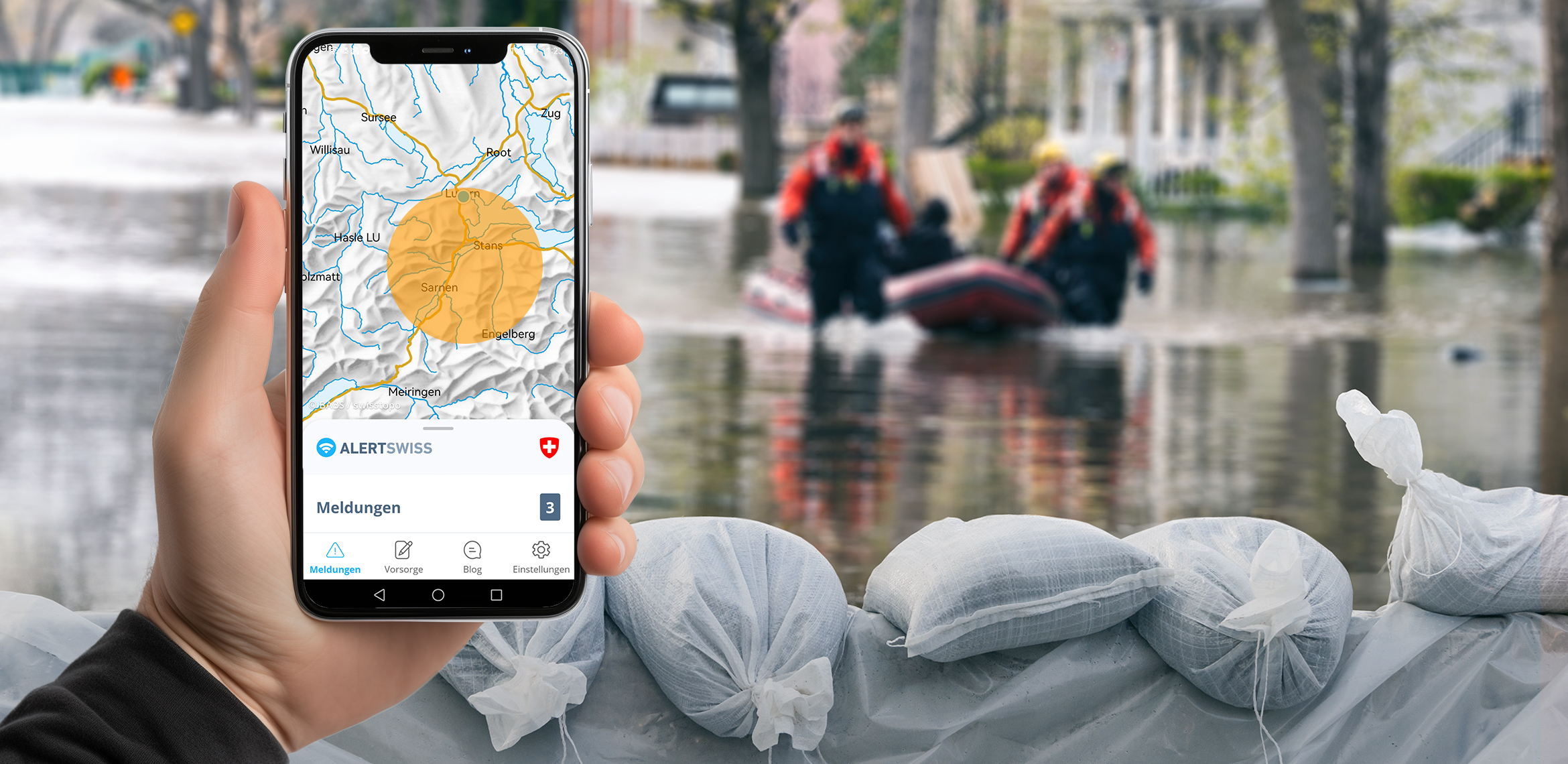 Ein Handy zeigt die Alertswiss-App mit einem Warnkreis. Im Hintergrund sind eine Überschwemmung, Sandsäcke und Rettungskräfte in einem Schlauchboot zu sehen.