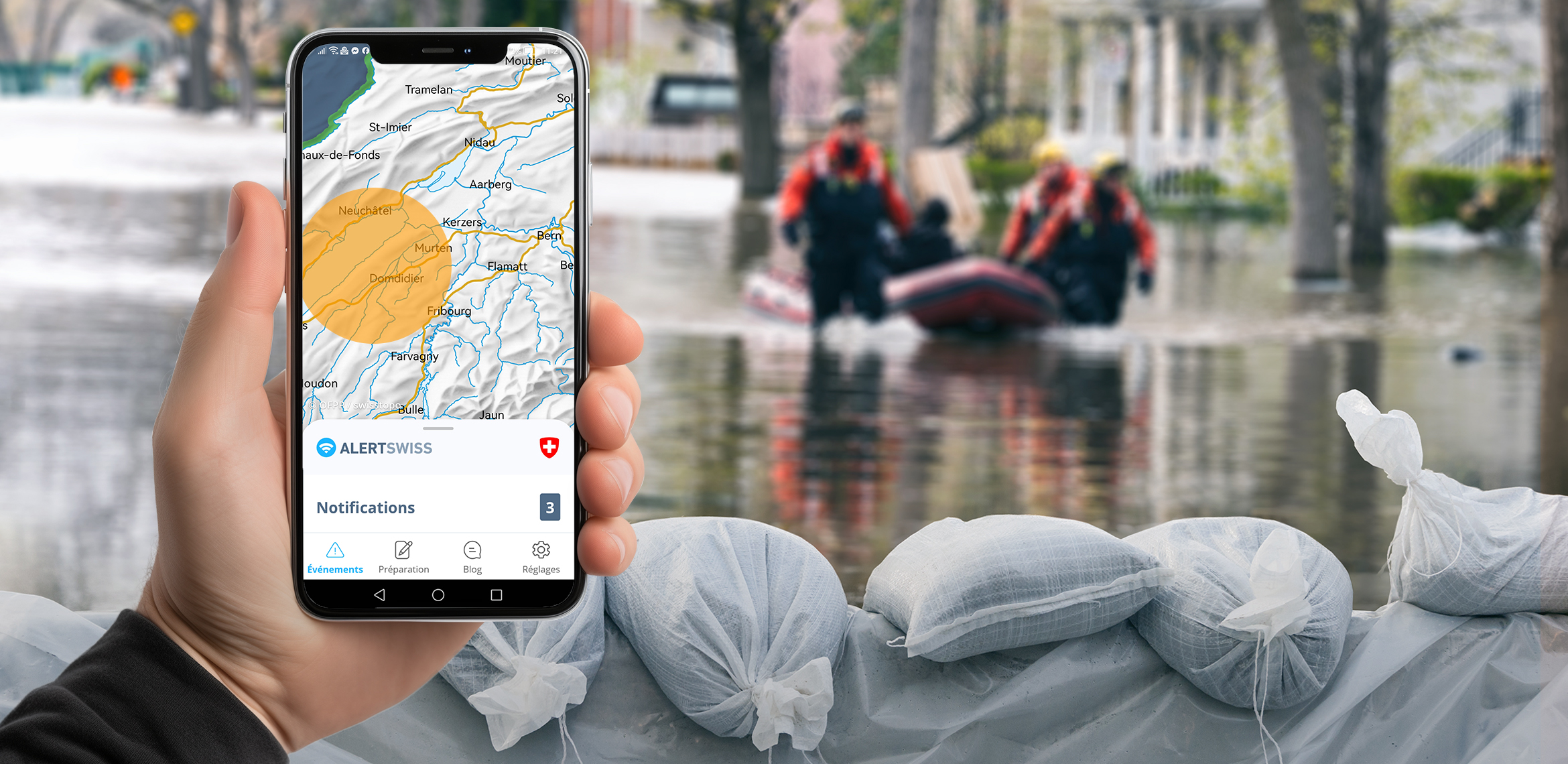 Un téléphone portable affiche un cercle d’avertissement sur l’application Alertswiss. En arrière-plan, on voit une inondation, des sacs de sable et des secouristes dans un canot pneumatique.