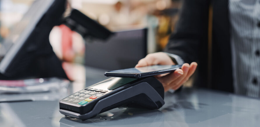 Eine Person bezahlt kontaktlos mit dem Smartphone am Terminal eines Geschäfts.