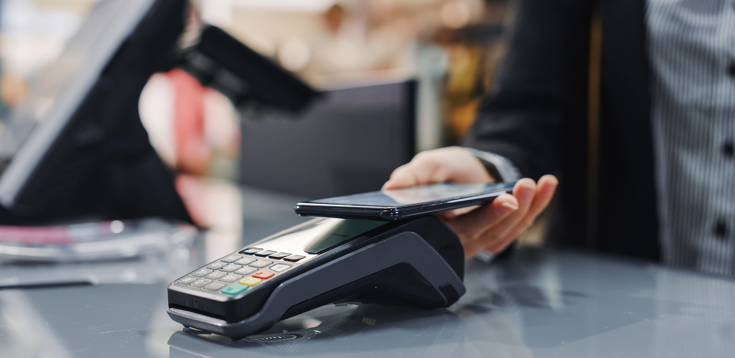 Eine Person bezahlt kontaktlos mit dem Smartphone am Terminal eines Geschäfts.