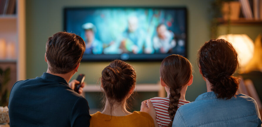 Eine Familie sitzt auf dem Sofa vor einen grossen Fernseher und streamt eine Serie.