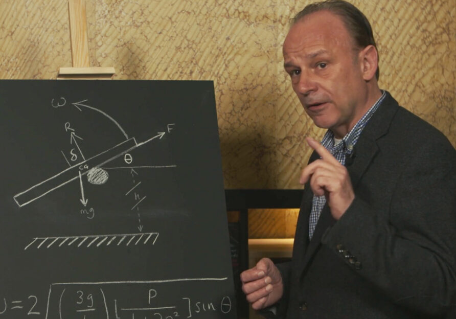 Der britische Physiker Robert Matthews steht vor einer Wandtafel mit einer Skizze und einer mathematischen Formel, die seine Forschung veranschaulichen.