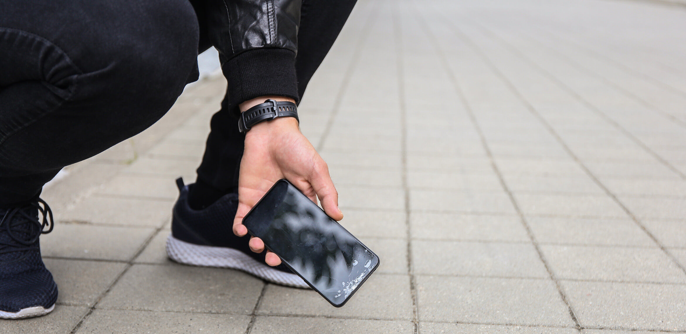 Eine Person hebt ein Smartphone mit gesprungenem Bildschirm vom Boden auf.