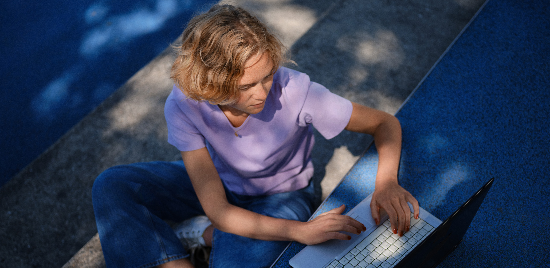 Une jeune personne est assise à l'extérieur devant son ordinateur portable.