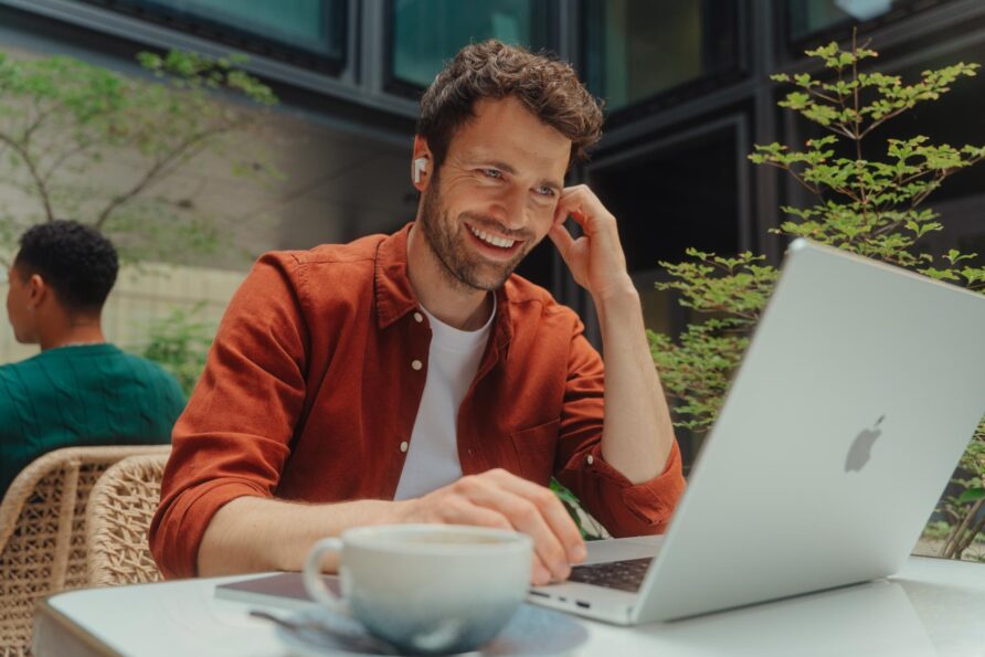 Un homme souriant est assis devant son ordinateur portable dans un café.