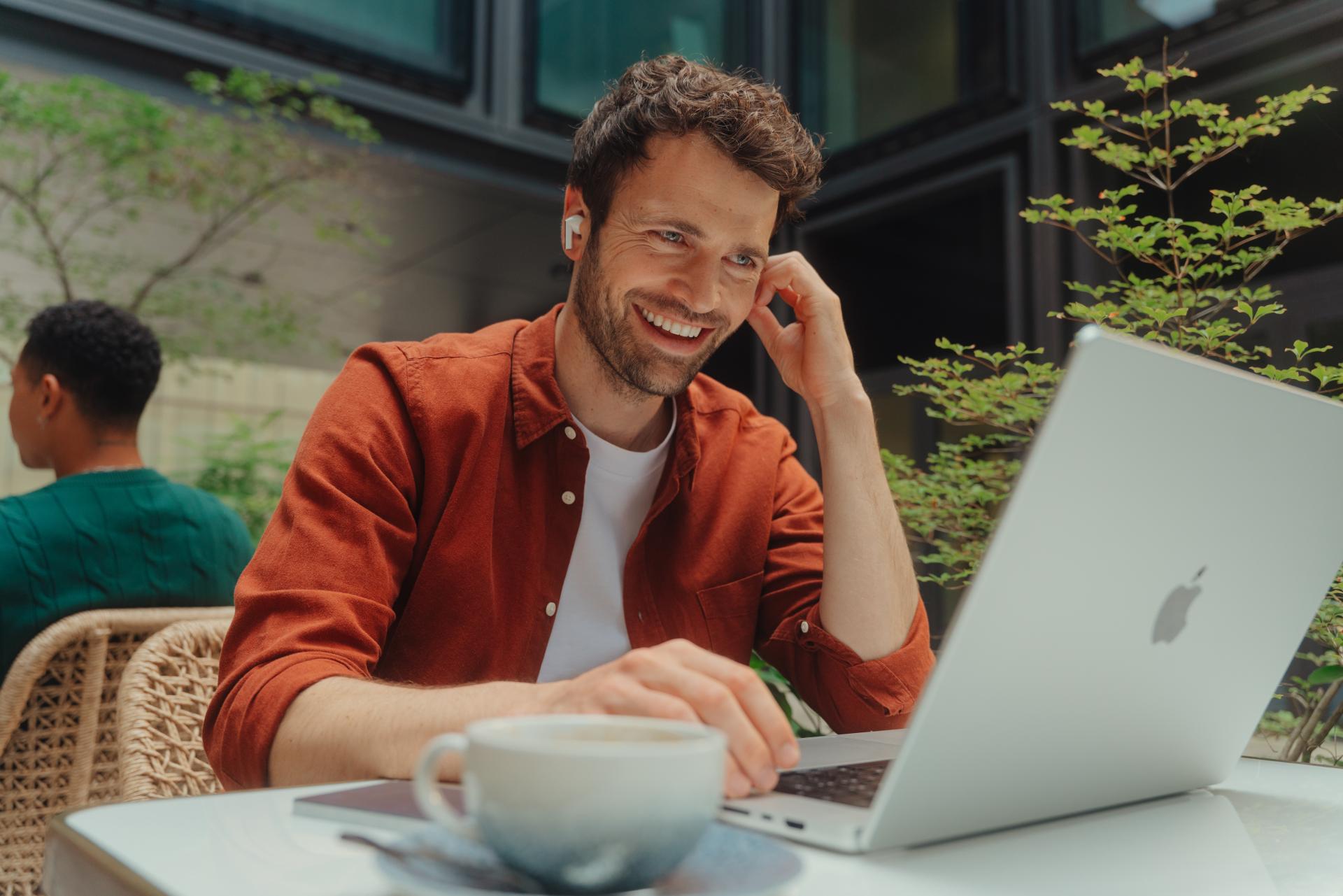 Un homme souriant est assis devant son ordinateur portable dans un café.