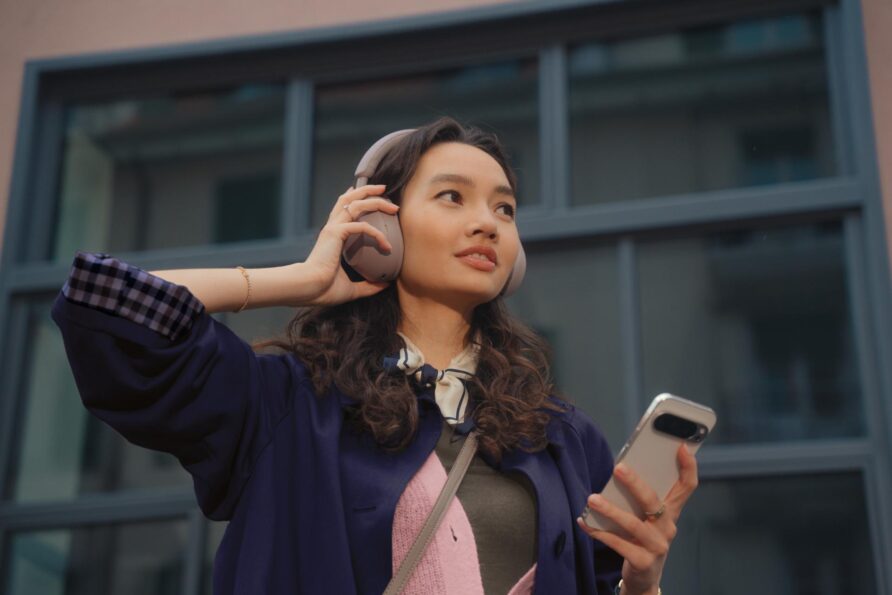 Une femme avec des écouteurs tient un smartphone dans sa main et regarde au loin.
