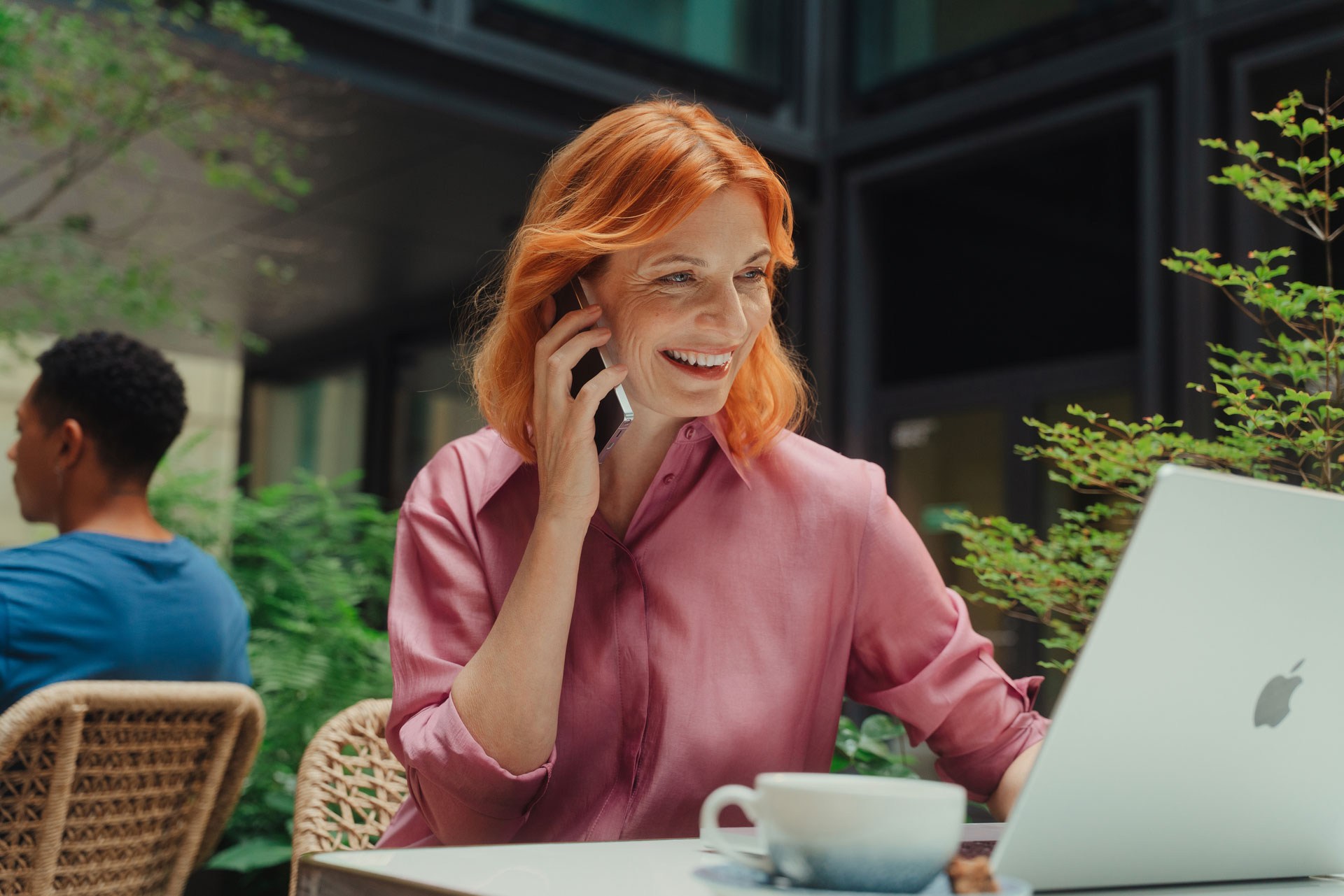 Ein Frau sitzt lächelnd an ihrem Laptop in einem Café.