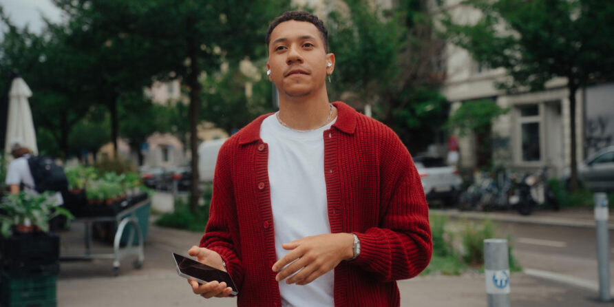 Ein Mann geht mit dem Handy in der Hand durch eine urbane Umgebung.