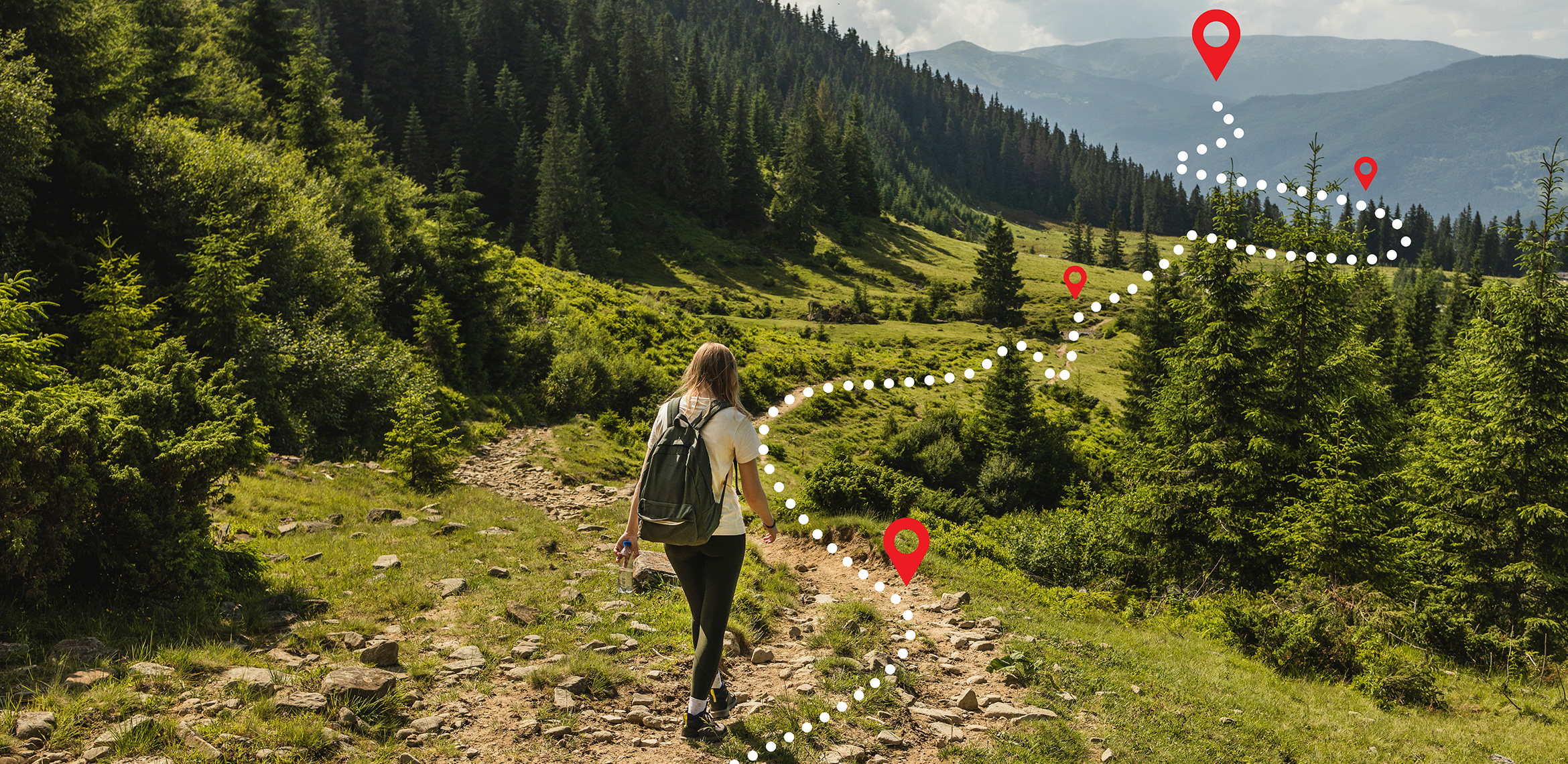 Eine Frau ist auf einem Wanderweg in den Bergen neben einem Wald unterwegs. Dabei hilft ihr eine digitale Anzeige.