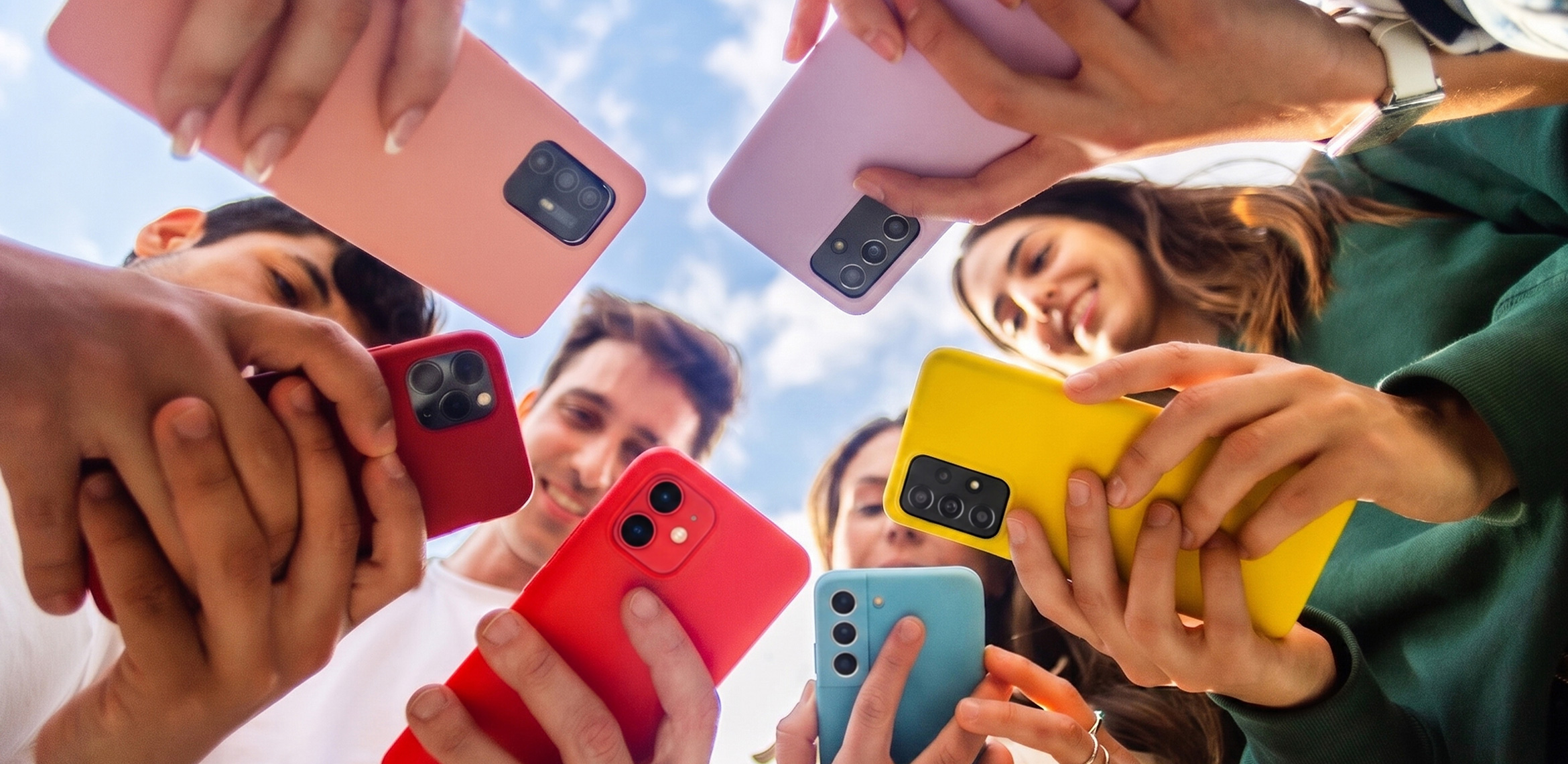 Eine Gruppe junger Menschen teilt unter freiem Himmel Inhalte auf ihren Smartphones mit bunten Hüllen.