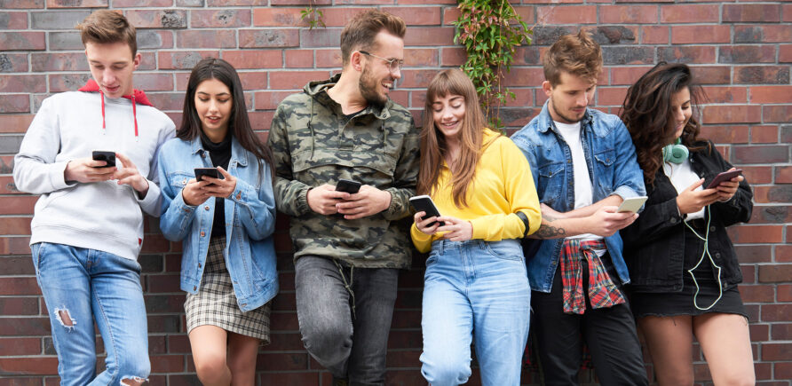 Junge Personen stehen an einer Wand und blicken auf ein Smartphone.