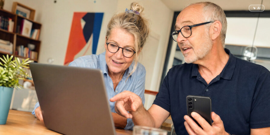 Zwei Senioren sitzen am Tisch und besprechen etwas am Laptop.