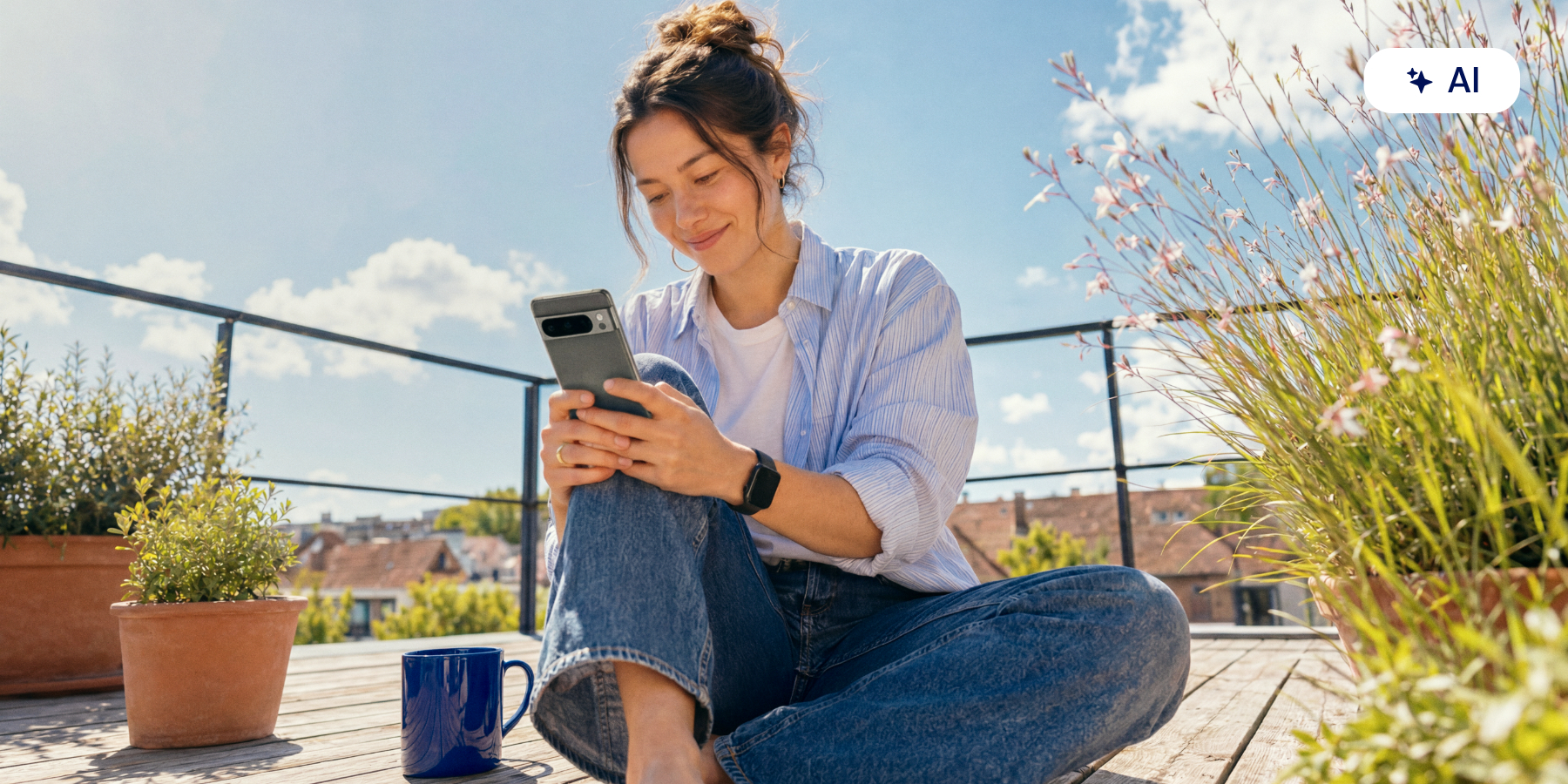 Person sitzt auf einer sonnigen Dachterrasse und nutzt ein Smartphone.